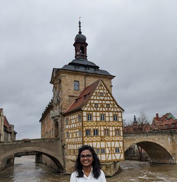 Sreehita smiles into the camera, in the background you can see an old half-timbered house in Bamberg.