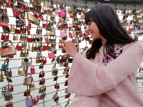 Rumeng stands by a kind of fence with lots of love locks attached.