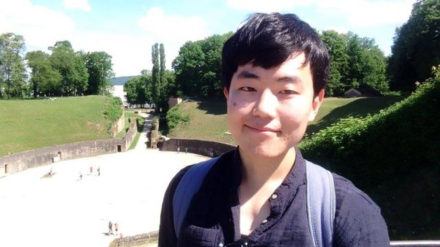 Jun smiles into the camera, a historic ampitheater can be seen in the background.