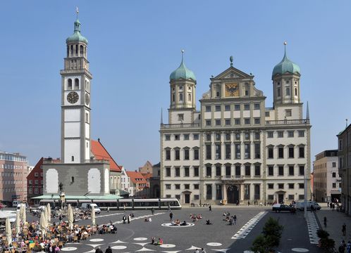 Blick auf das Augsburger Rathaus und den Rathausplatz, auf dessen Backsteinboden viele Studierende sitzen. © Medien- und Kommunikationsamt der Stadt Augsburg