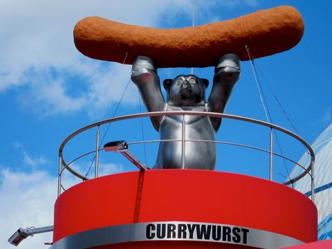 Auf dem Dach des Currywurst Museum hält ein silberner Berliner Bär eine Currywurst über seinem Kopf.