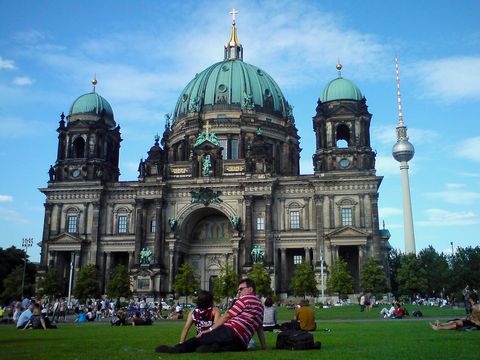 Passers-by and students sit on the lawn of the Lustgarten in front of the Berlin Cathedral in summer.