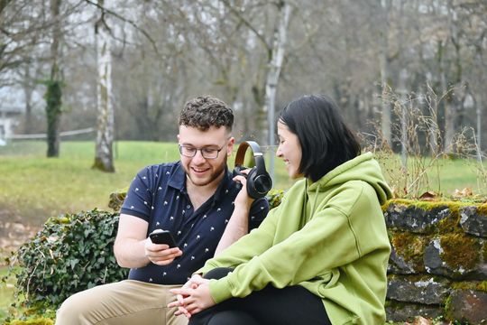 Jinmeng and Chistos sitting in a park listening to music on a phone and headset