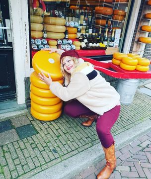 Lilit poses with a tall stack of cheese wheels in the streets of Amsterdam.
