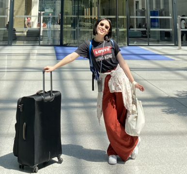 A picture of Jinmeng with sunglasses, backpack and suitcase in front of the Frankfurt airport.