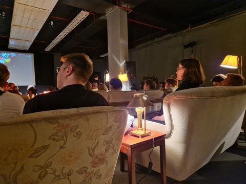 Visitors to the film festival sit on sofas in a darkened room and listen to a lecture.