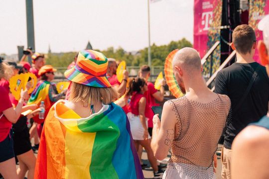 two people in a pride parade, one wearing a rainbow flag