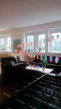 View into a student dormitory: You can see a sofa and a table football table, the room is decorated with a garland with flags of different countries hanging on it.