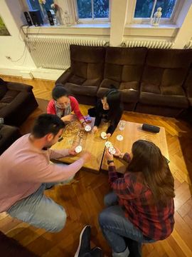 Students sit on the floor around a table and laugh and play a card game together.