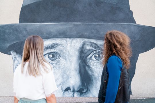 two people standing in front of mural showing upper part of Joseph Beuy's head