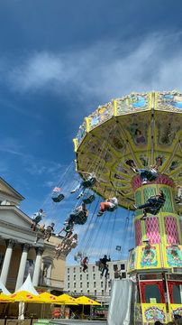 A swing carousel in full swing at the Darmstadt Heinfest. People are sitting in the swings, the sky is blue and the sun is shining.