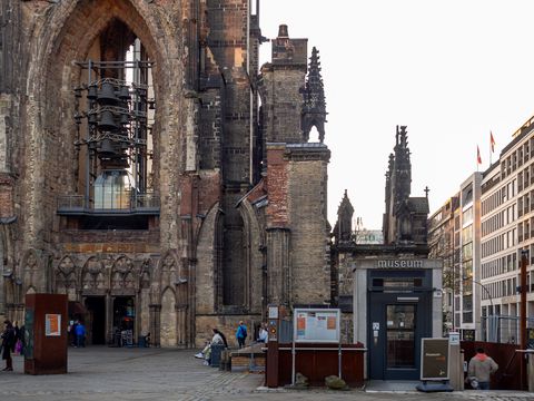 A visitor entering St. Nikolai museum via its entrance in the foreground, while a few other sit and stand near the tower in the background.