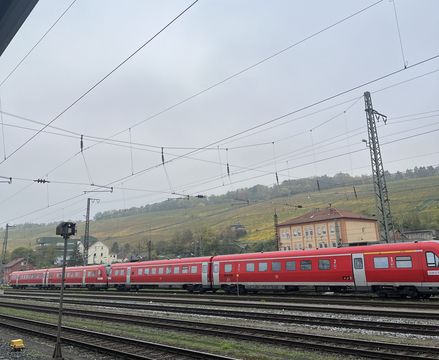 You can see tracks and trains in the foreground. The weather is grey and foggy, and you can see vineyards rising in the distance.