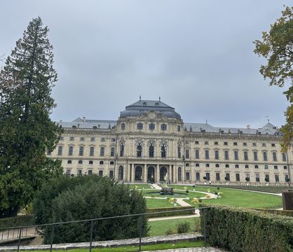 You can see the Würzburg Residence. The weather is grey and foggy. In the foreground you can see the green and well-kept park of the residence.