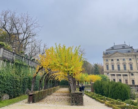 You can see the Würzburg Residence. The weather is grey and foggy. In the foreground you can see the green and well-kept park of the residence.