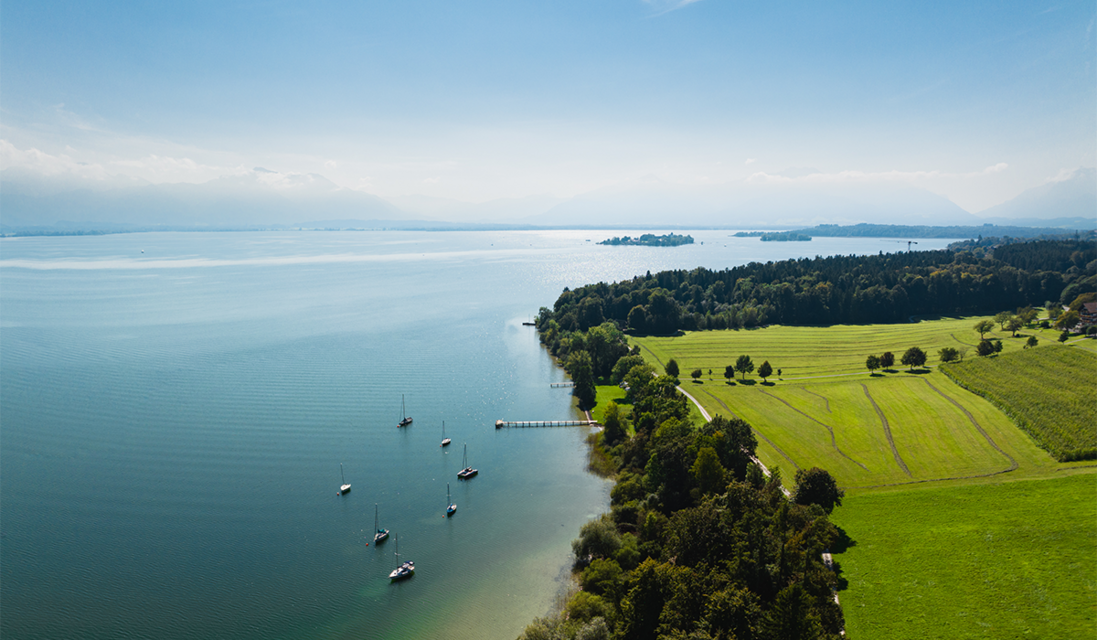 Shoot from the air of the shore of lake Chiemsee. Lush green nature and blue water. In the distance the islands can be spotted.