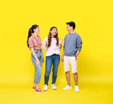 Drei Studierende stehen vor einem gelben Hintergrund
